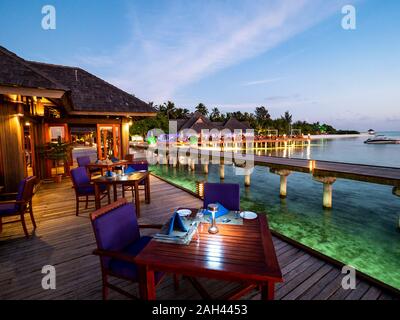 Les Maldives, table de salle à manger du restaurant côtières au crépuscule avec pier en arrière-plan Banque D'Images