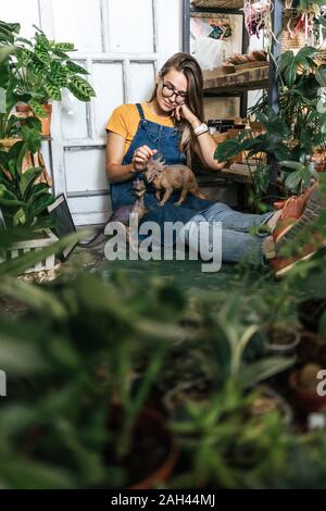 Jeune femme avec figurine dinosaure assis sur le plancher d'une petite boutique avec des plantes Banque D'Images