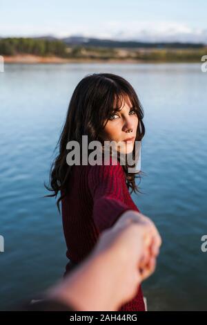 Jeune femme tenant la main d'un homme, debout au bord du lac Banque D'Images