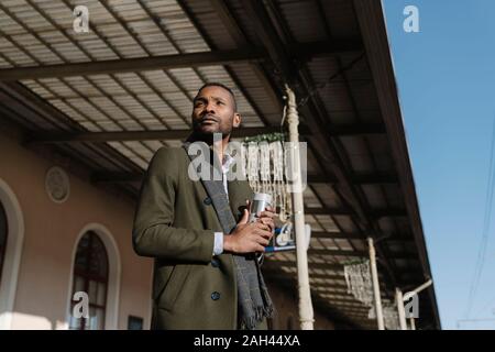 L'homme élégant avec tasse réutilisable attendant le train Banque D'Images