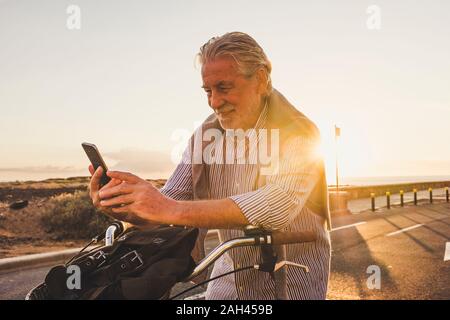 Senior du smartphone sur le vélo au coucher du soleil, Tenerife Banque D'Images