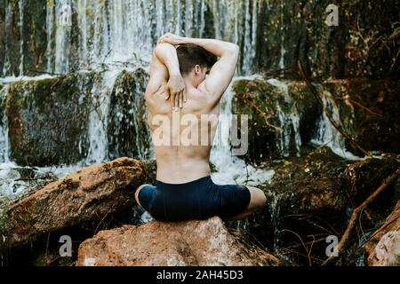 Vue arrière du jeune homme pratiquant le yoga sur une cascade Banque D'Images