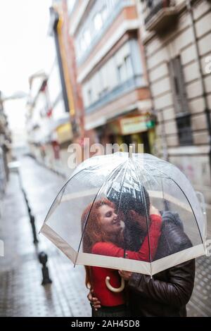 Couple in love kissing sous parapluie transparent dans la ville Banque D'Images