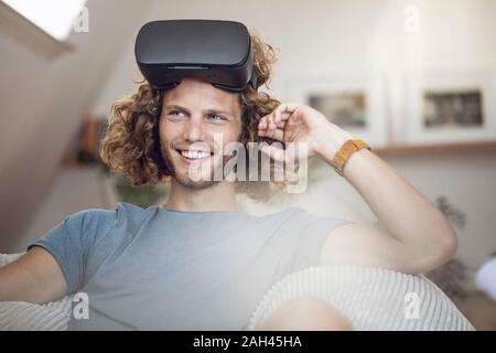 Portrait of smiling young man wearing VR lunettes à la maison Banque D'Images