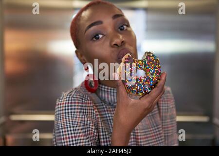 Jeune femme manger un donut dans un ascenseur Banque D'Images