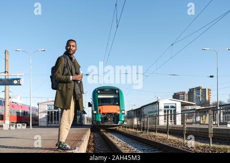 Portrait de l'homme élégant avec tasse réutilisable attendant le train Banque D'Images