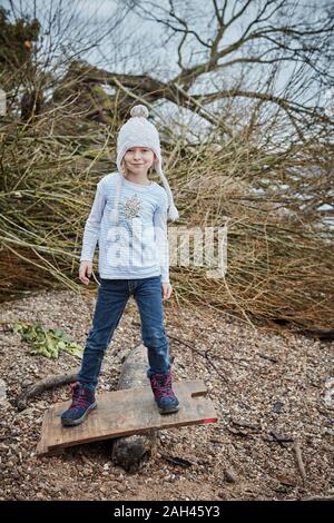 Portrait of smiling little girl wearing bobble hat en équilibre sur seesaw Banque D'Images