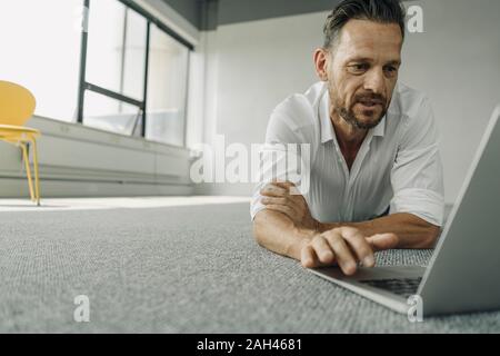 Mature businessman allongée par terre dans le bureau vide using laptop Banque D'Images