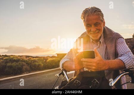 Senior du smartphone sur le vélo au coucher du soleil, Tenerife Banque D'Images