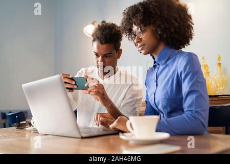 Les élèves à l'aide d'ordinateur portable pour un projet dans un café, prendre une photo Banque D'Images