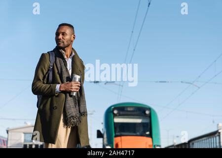 Portrait de l'homme élégant avec tasse réutilisable attendant le train Banque D'Images