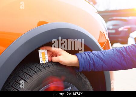 L'examen de technicien pneu de voiture avec un instrument de mesure dans une station-service. Mesures mécanicien avec profiler la profondeur de sculpture. Banque D'Images