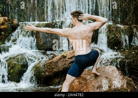 Vue arrière du jeune homme pratiquant le yoga sur une cascade Banque D'Images