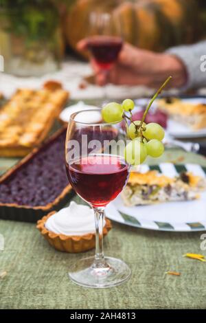 Un verre de vin sur une table de fête dans le jardin sur un fond de tarte, et les mains d'une femme âgée. Concept de vacances en famille. Banque D'Images