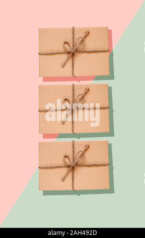 Eco-friendly présente trois dans une des boîtes en carton décorée d'un noeud sur corde et vert sur fond rose pastel Banque D'Images