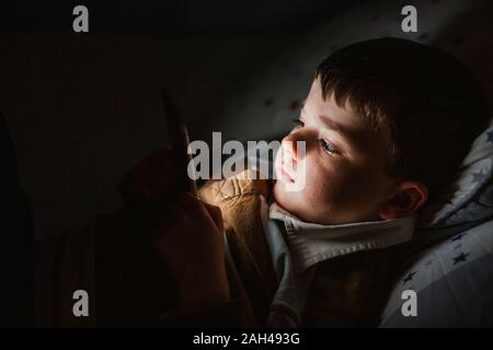 Portrait du petit garçon au lit en utilisant smartphone à nuit Banque D'Images