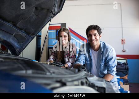 Jeune femme et homme debout près de voiture en service centre smiling at camera et de travailler en équipe Banque D'Images