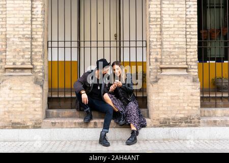 Young couple sitting on stairs looking at smartphone Banque D'Images