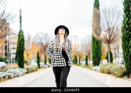 Smiling businesswoman wearing hat and sunglasses, looking up Banque D'Images