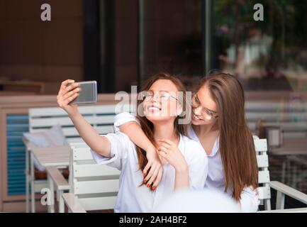 Cheerful female friends prenant en photo selfies cafe. Deux belles jeunes femmes de sourire et à la recherche de l'appareil photo de smartphone. Concept d'amitié Banque D'Images