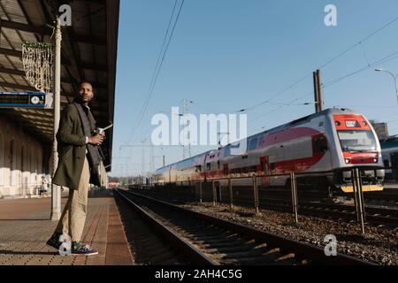 L'homme élégant avec tasse réutilisable attendant le train Banque D'Images