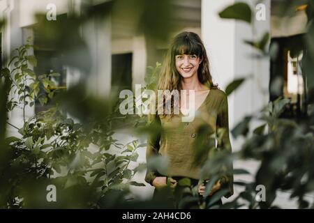 Portrait of smiling brunette woman derrière les plantes Banque D'Images