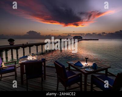 Les Maldives, table de salle à manger du restaurant côtières au crépuscule avec pier en arrière-plan Banque D'Images