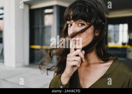 Portrait of smiling brunette woman, doigt sur la bouche Banque D'Images