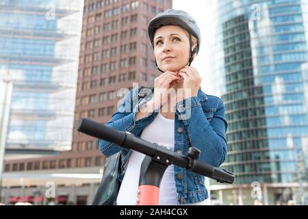 Femme avec l'e-scooter dans la ville mise sur casque, Berlin, Allemagne Banque D'Images