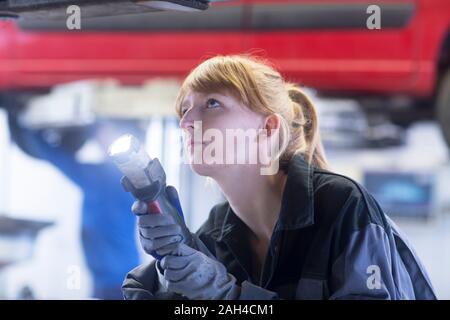 Mécanicien automobile féminin avec lampe à la recherche de fond d'un garage de réparation de voiture Banque D'Images