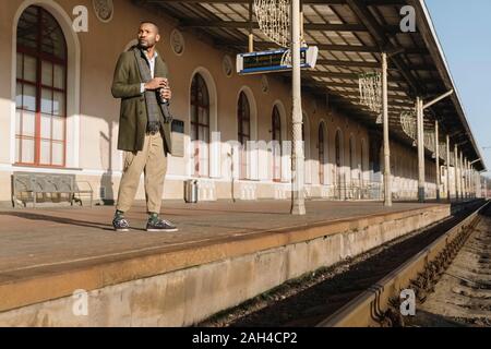 L'homme élégant avec tasse réutilisable attendant le train Banque D'Images