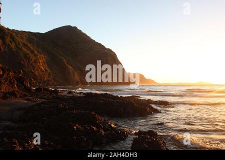 Lever du soleil à partir de la plage de Whatipu à distance à l'égard Manukau Harbour dans les Waitakere Ranges de Auckland, Nouvelle-Zélande, avec ciel bleu clair et les falaises Banque D'Images