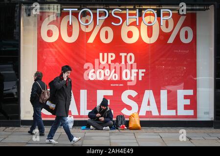 Le centre de Londres, Londres, le 24 décembre 2019. Un homme est assis avec quelques effets personnels sur la chaussée, en dehors d'une publicité boutique ventes de Noël la veille de Noël. Le nombre de ménages sans-abri nouvellement a augmenté au cours des 12 derniers mois, et à Londres, le problème croissant est particulièrement visible avec le nombre de sans-abri ayant grimpé à de nouveaux sommets. Credit : Imageplotter/Alamy Live News Banque D'Images