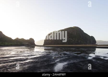 Tôt le matin à la plage de sable noir Whatipu dans les Waitakere Ranges de West Auckland, Nouvelle-Zélande. Il y a des montagnes de Steep Rock reflète dans l'eau. Banque D'Images