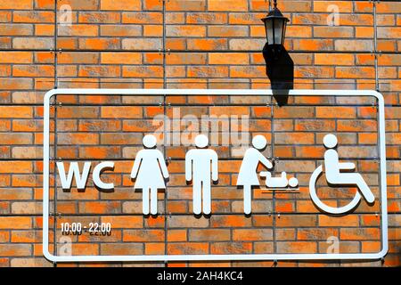 Sur le mur de brique orange est un panneau toilettes avec blanc des WC, un homme, une femme, une scène d'un change bébé bébé et une personne en fauteuil roulant. Banque D'Images