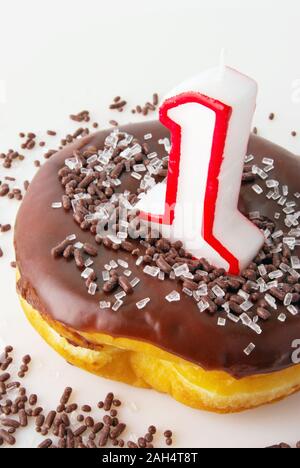 Un noir Chocolat glacé donut avec un certain nombre une bougie dans le trou de beigne. L'anneau est recouvert de paillettes. Banque D'Images