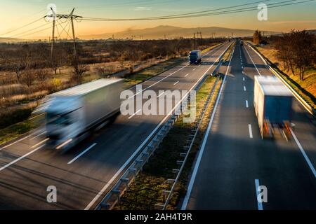 Les camions de livraison en conduite à grande vitesse sur une route à travers le paysage rural. Blurred motion rapide en voiture sur l'autoroute. Scène de fret sur l'autoroute Banque D'Images