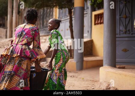 Deux Filles Africaines Transportant Un Seau D'Eau Lourde À La Maison De La Station De Pompage Banque D'Images