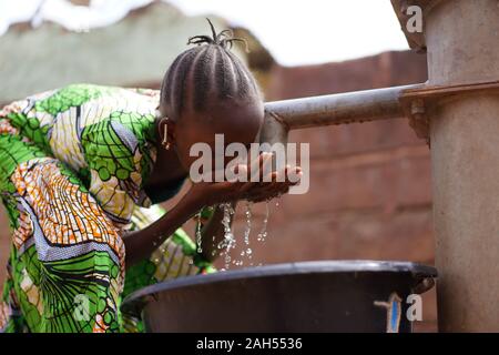 Gentiment Braided African Girl Laver Son Visage Avec De L'Eau Douce Au Borehole Banque D'Images