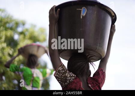 Backshot d'une jeune fille africaine portant de lourdes réservoir d'eau Retour à l'accueil du village de forage Banque D'Images