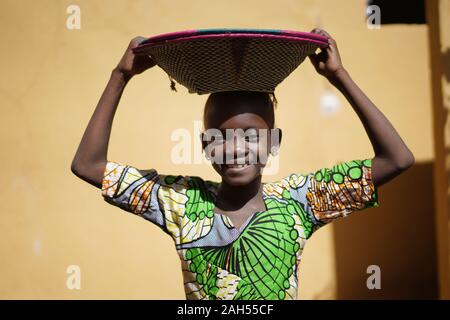 Jolie petite fille africaine portant un panier de paille à la main autant sur la tête. Banque D'Images