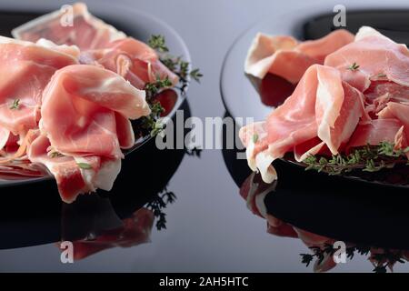 Le Prosciutto au thym sur une plaque noire. Fond réfléchissant noir. Banque D'Images