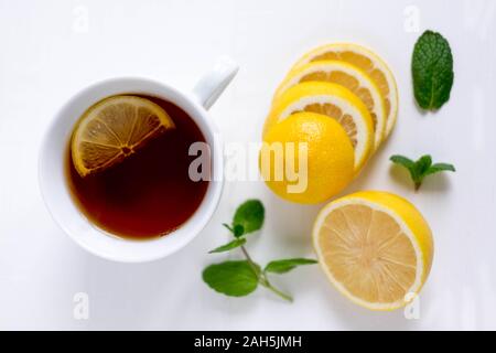 Magnifique photo de thé noir dans une tasse blanche avec une rondelle de citron et menthe sur fond clair. Banque D'Images