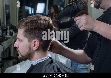 Close-up. Master coiffure blow-drys un jeune mec dans un salon de coiffure. Soins pour les cheveux des hommes. La beauté des hommes. Coupe de cheveux et de coiffure Banque D'Images