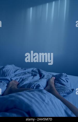 Libre les jambes des femmes sont en beige literie en chambre cosy. Matin tranquille et paresseux concept, copy space, verticale, avec des tons de couleur bleu classique Banque D'Images