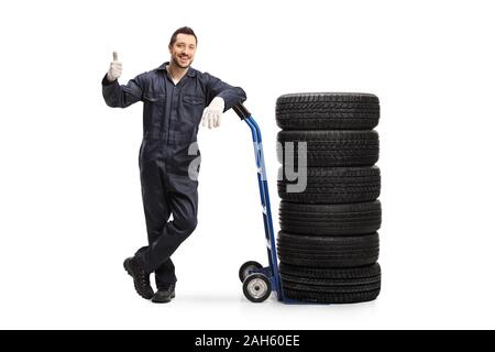 Portrait d'un mécanicien d'automobile s'appuyant sur un camion de main avec pneus et showing Thumbs up isolé sur fond blanc Banque D'Images