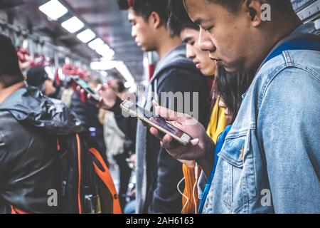 Hong Kong, Chine - Novembre 2019 : les gens à la recherche sur téléphone mobile à l'intérieur du train / métro MTR à HongKong Banque D'Images