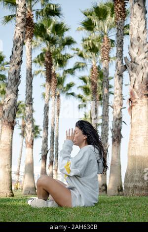 la fille assise sur l'herbe verte parmi beaucoup de palmiers les arbres médite et se détend Banque D'Images