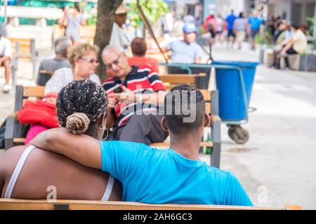 Les gens de La Havane - un jeune couple au premier plan, tandis qu'un couple plus âgé est assis ensemble dans l'arrière-plan ; dans un parc. Banque D'Images