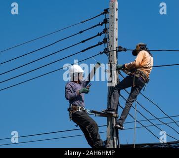 Chiang Mai, Thaïlande, décembre, 15, 2019 : deux travailleurs en place un pôle travaillant sur des fils et des câbles dans la rue en Thaïlande contre un ciel bleu clair. Banque D'Images